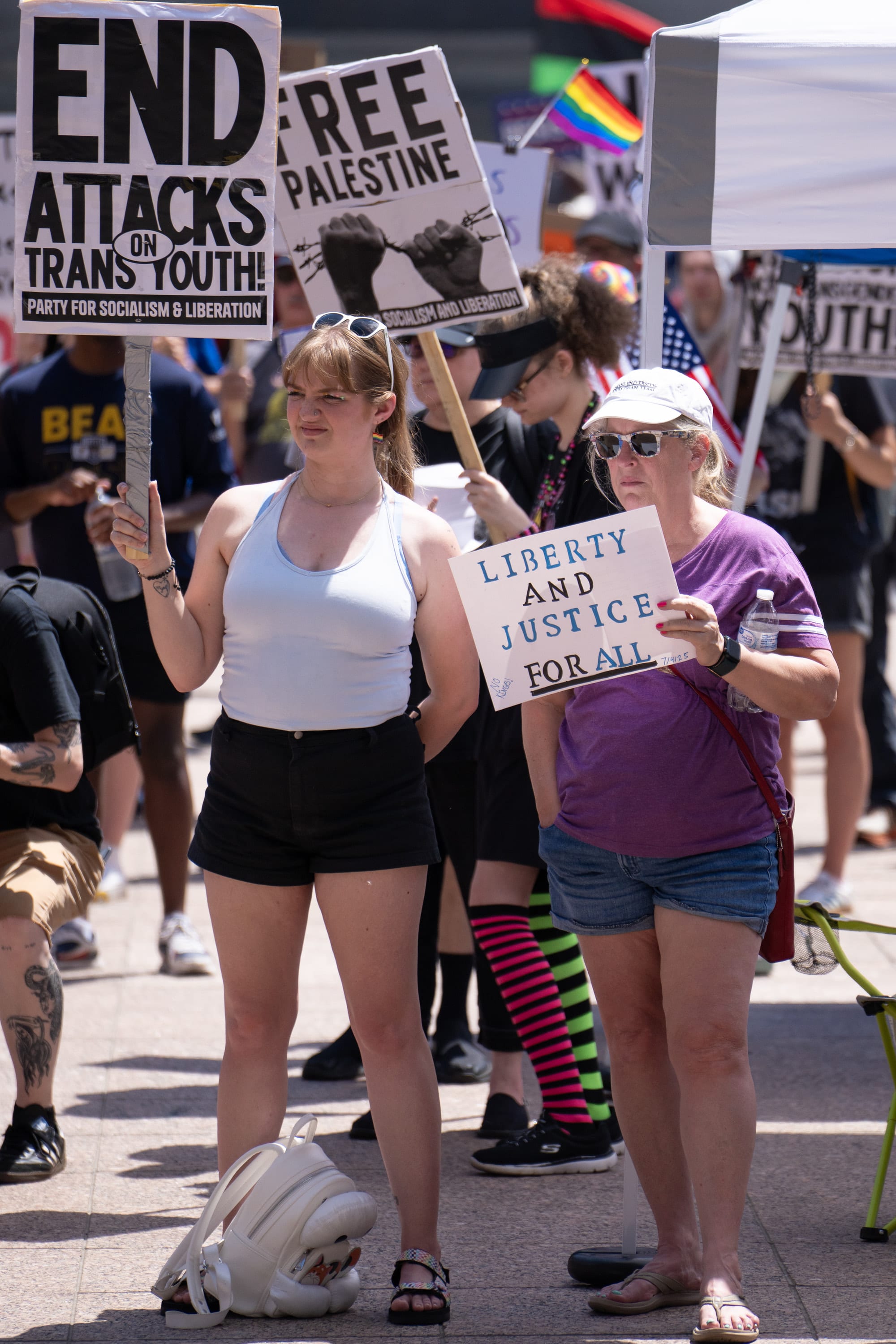 Two women stand among signs reading 'End attacks on trans youth', 'Free Palestine' and 'Liberty and justice for all'.