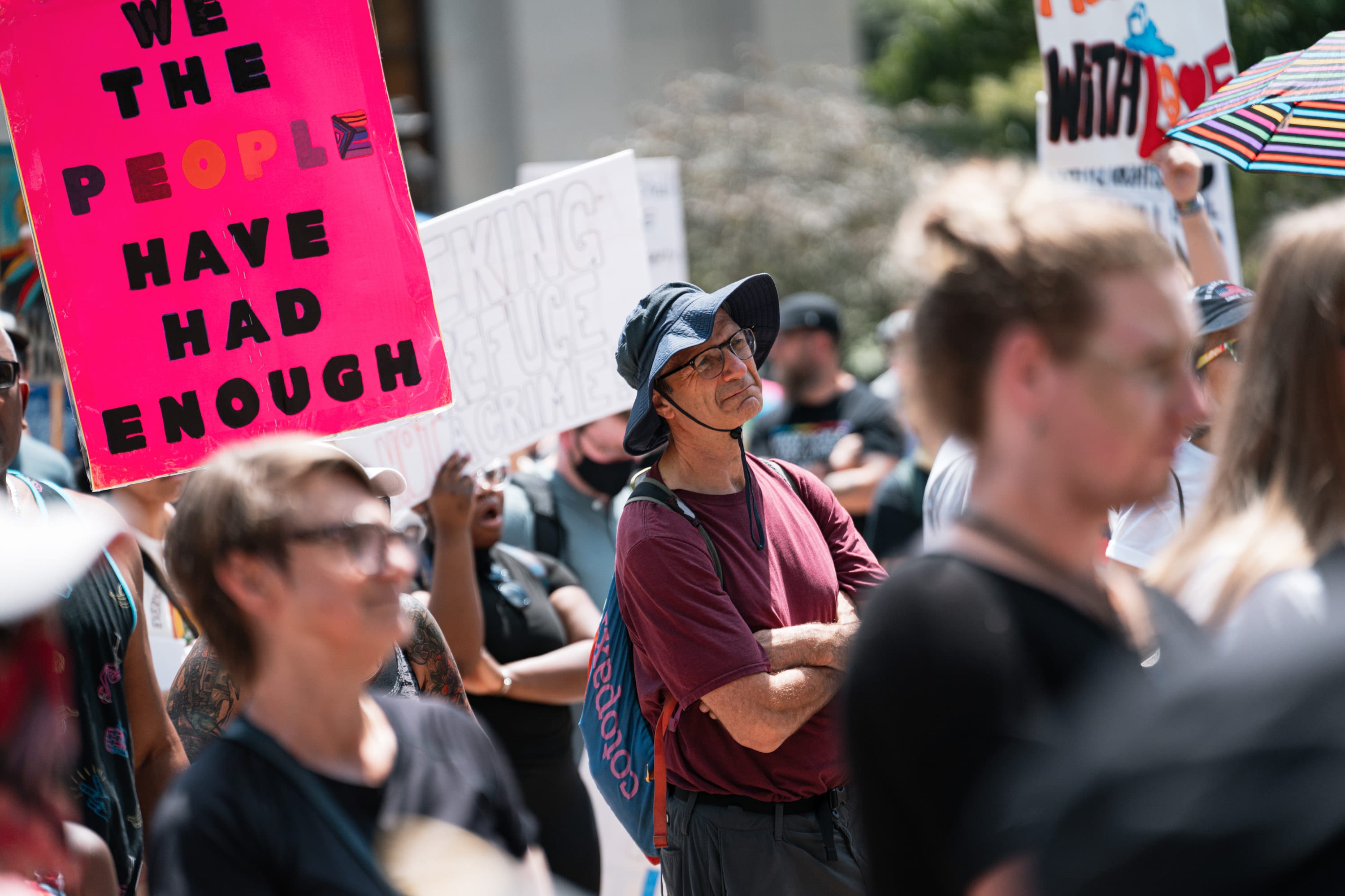 People in the crowd listen beneath a pink sign reading 'We the people have had enough'.