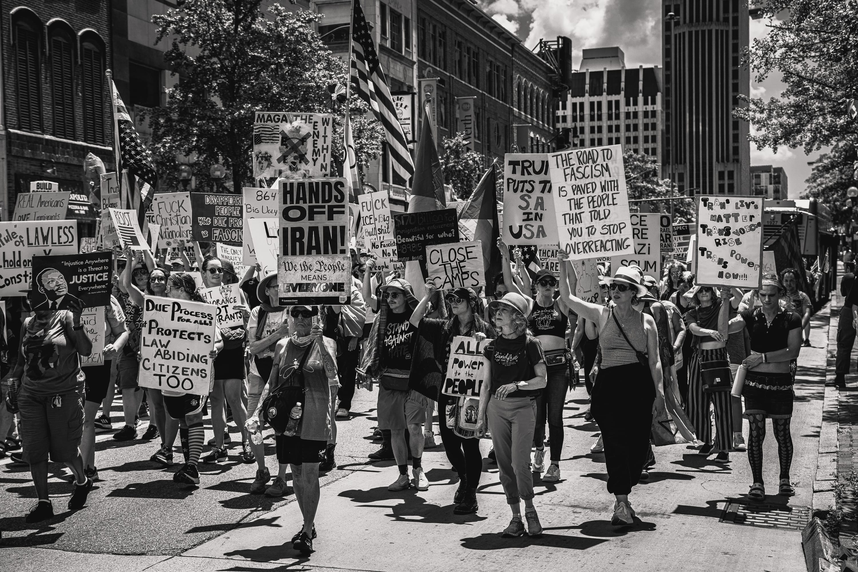 Black and white: the march fills a downtown street, signs held high between tall buildings.