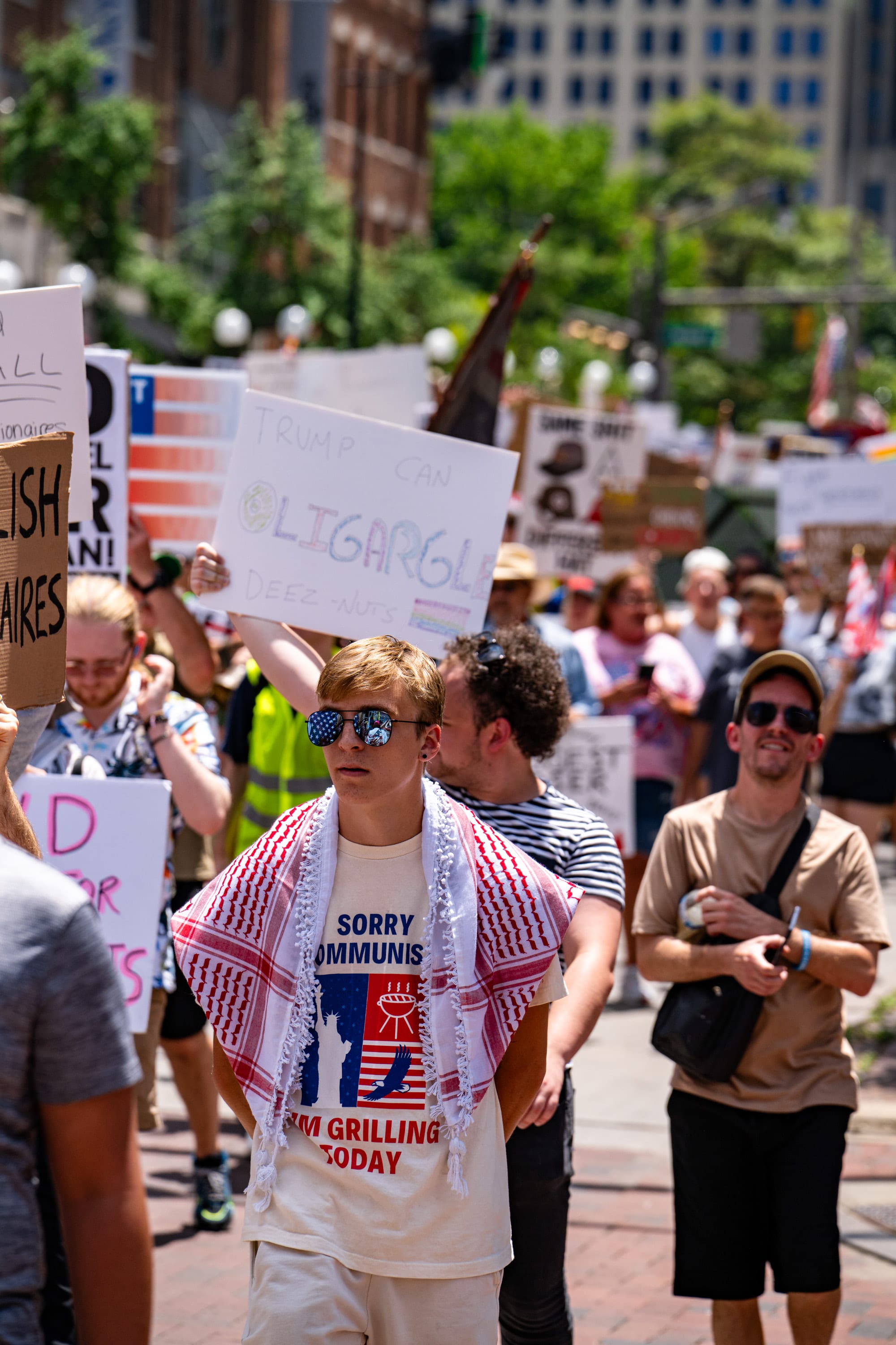 A young man in sunglasses, a red keffiyeh over his shoulders, walks with the march.