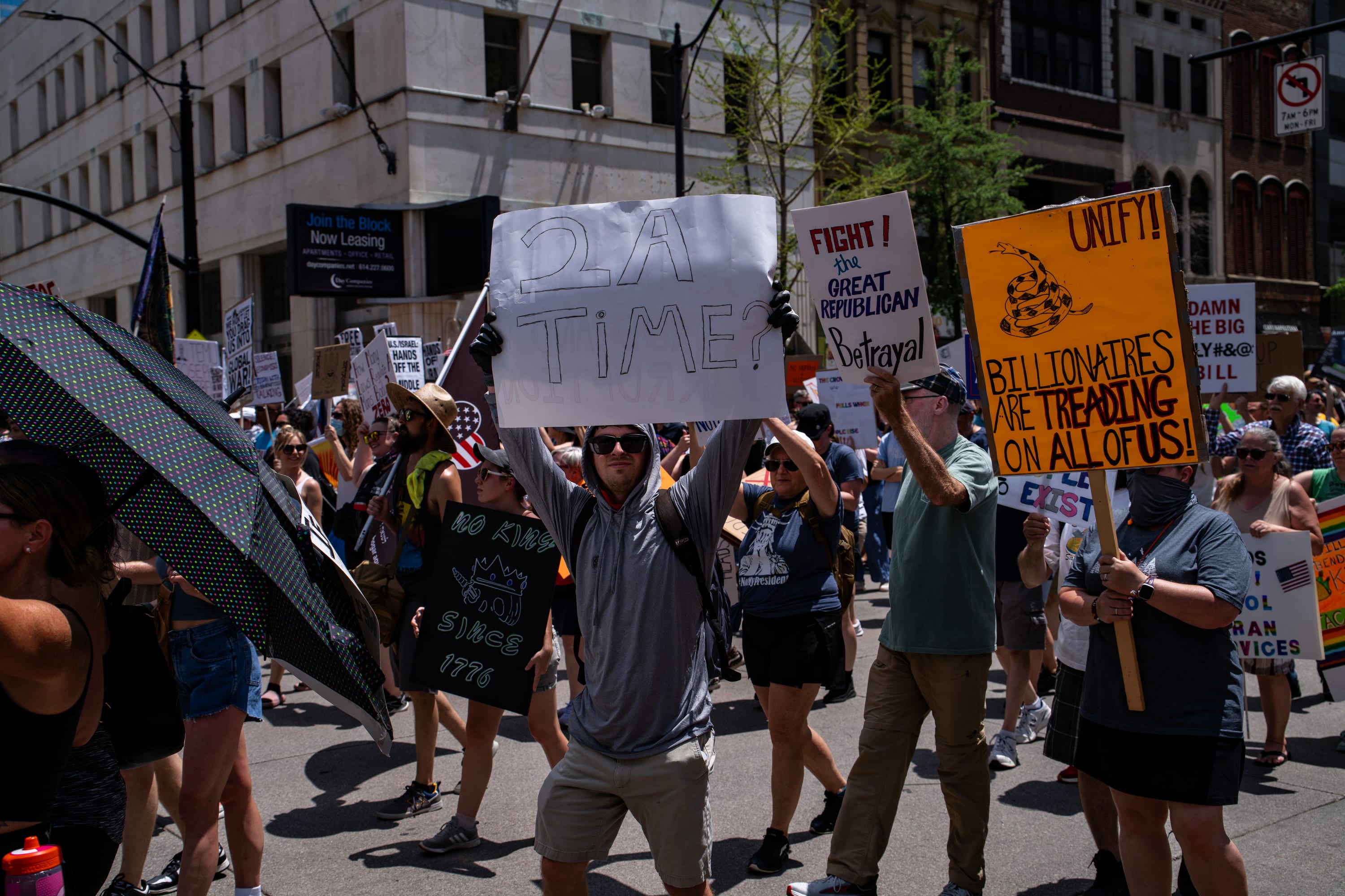Marchers fill the street, a yellow 'Billionaires are treading on all of us' flag among the signs.