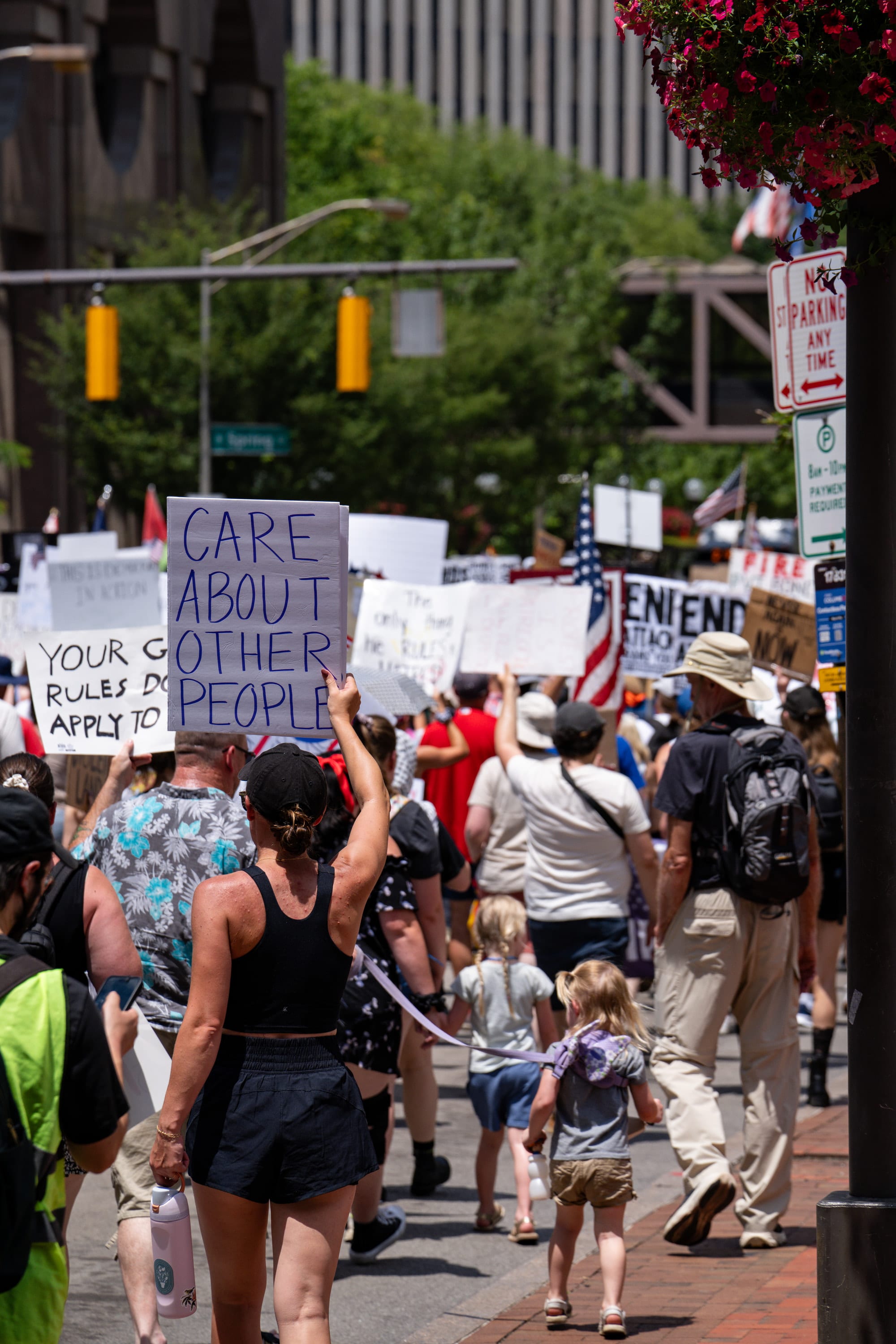 The march stretches up a tree-lined street, a sign reading 'Care about other people' above the crowd.