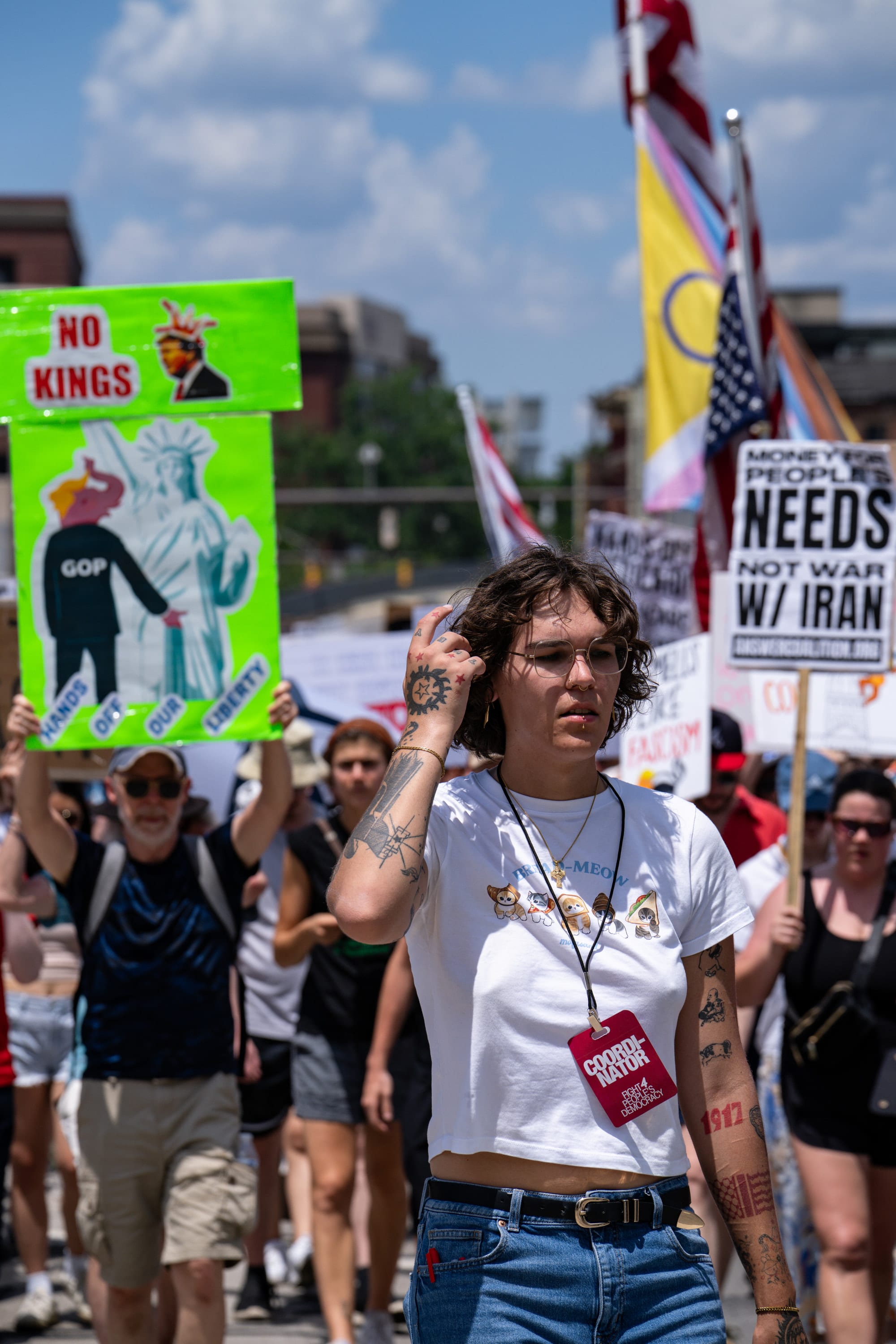 A woman with tattooed arms walks at the front of the march beneath a 'No kings' sign.
