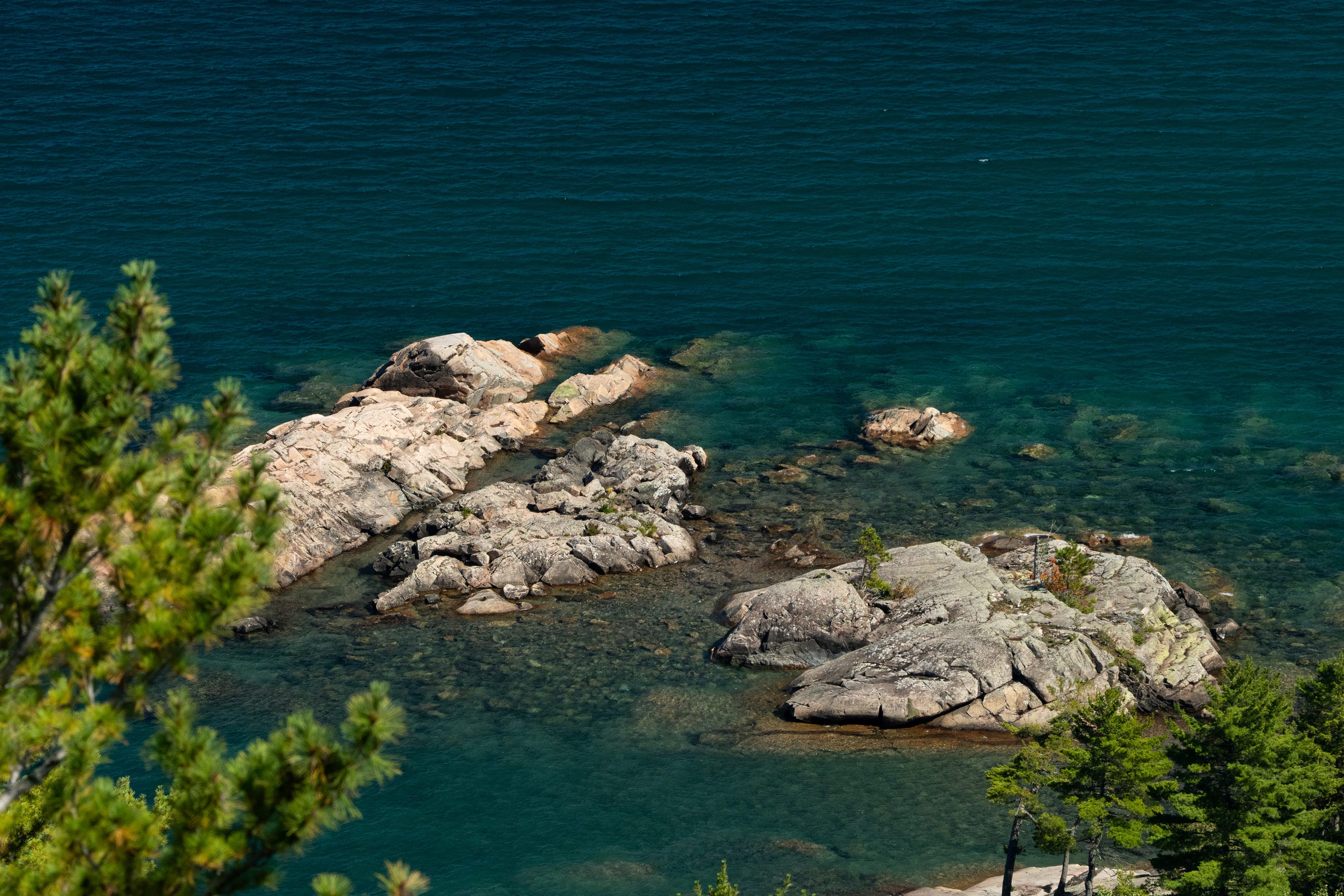 Pink granite boulders in clear green water below pine branches.