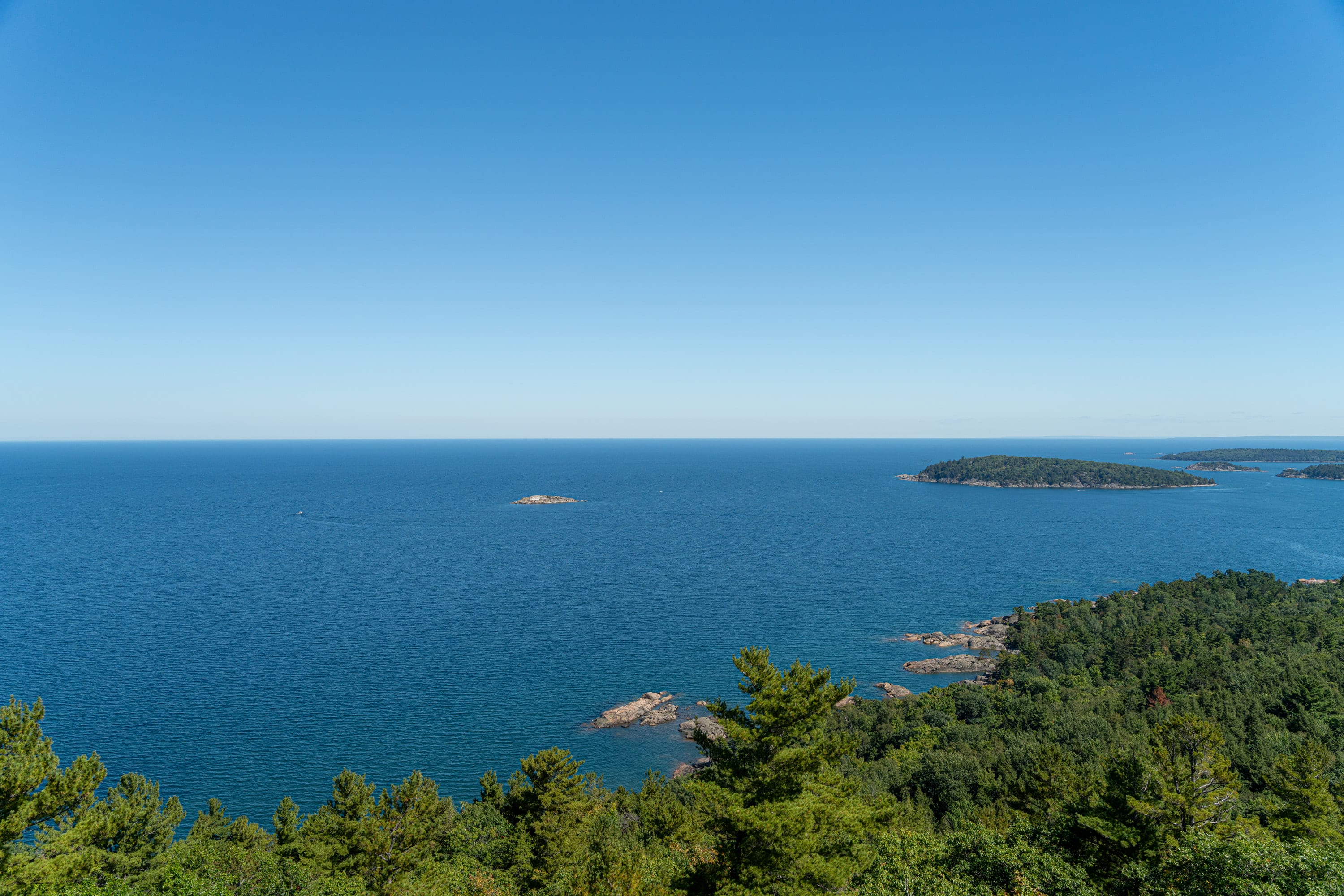 Open water to the horizon, wooded islands and rocks off a forested point.