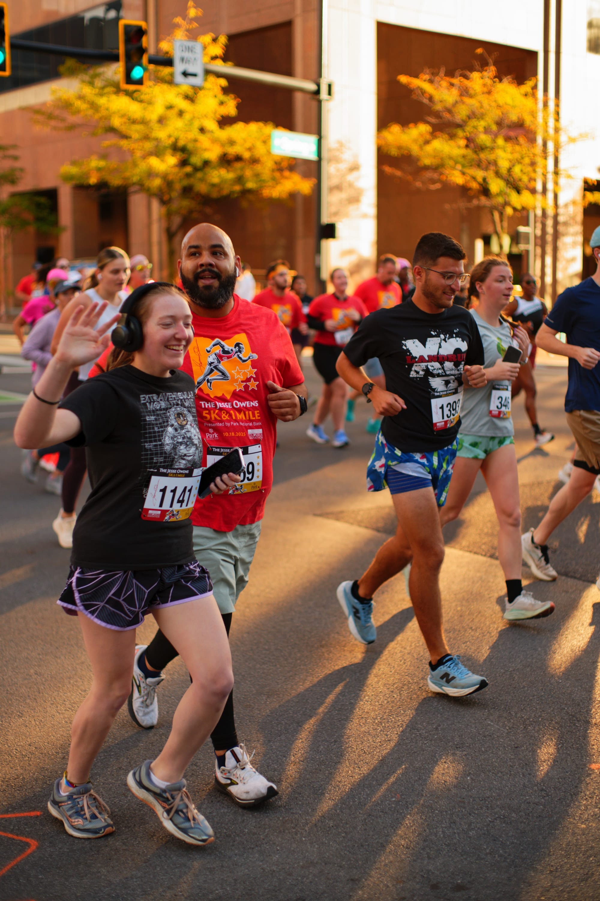 Runners laugh and wave at the camera as they pass in the early light.